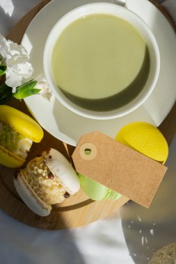 Kağıt not uzay şablonunu kopyala tatlı sarı makaron tatlı fincanı yeşil bitki bazlı kibrit çaylı latte sıcak sabah yatağı atmosferinde. Yaratıcı tatil romantik randevu fikri. Bitkisel prebiyotik lif