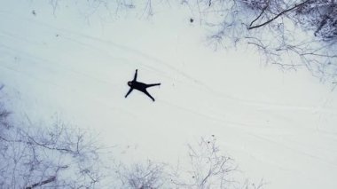 Adam uzanmış, kar meleği yapıyor. Açık hava aktiviteleri ve ekolojik turizm. Doğal kış mevsimi geçmişi. İHA 'nın karını kaplayan çam ağacının havadan görünüşü