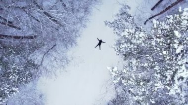 Adam uzanmış, kar meleği yapıyor. Açık hava aktiviteleri ve ekolojik turizm. Doğal kış mevsimi geçmişi. İHA 'nın karını kaplayan çam ağacının havadan görünüşü