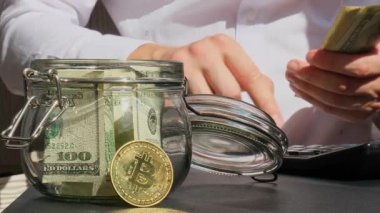 Bitcoin dijital altın. Uzman tüccarların elinde cam kavanozdan gelen dolar banknotlarını sayıyor. El ele tutuşup tanınmaz hale geliyor. Kazanılan ticaret grafikleri büyüme Kripto para birimi