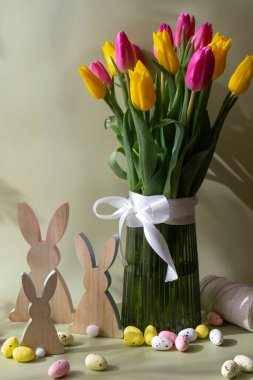 Mutlu Paskalya kompozisyonu ahşap tavşan yumurtaları. Pastel yeşil arka planda renkli lalelerden oluşan bir buket. Tebrik kartı için alanı kopyala. Tatil çiçekleri ilkbahar atmosferi