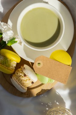 Boş mesaj kâğıdı fotokopisi: Besin zengini kibrit içeceği, ahşap tepside taze çiçeklerle süslü, modaya uygun makarna tatlısı. Günaydın güzel kahvaltı hediyesi fikri. Canlı, yaratıcı.