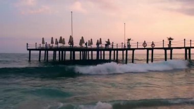 Gün batımında Antalya Türkiye 'deki ahşap iskeleye büyük dalgalar çarpıyor. Deniz seyahati turizmi konsepti. Kumsal sakinliği ve yavaşlama 