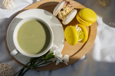 Tatlı sarı Makaron Tatlı Fincanı yeşil bitki bazlı kibrit çaylı latte, rahat bir sabah yatağı atmosferinde. Yaratıcı tatil romantik randevu fikri. Bitkisel prebiyotik fiber süper yiyecek. Antioksidan zengini.