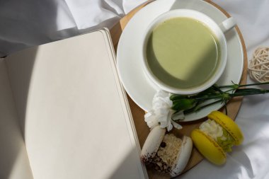 Yeşil latte kibrit, tatlı makarna ve dağınık yatağın üzerinde boş defter yansıma günlüğü. Tatil kahvaltısı çay içeceği kavramı. Sıcacık minimalist süper yiyecekler canlı renkler sağlıklı beslenme