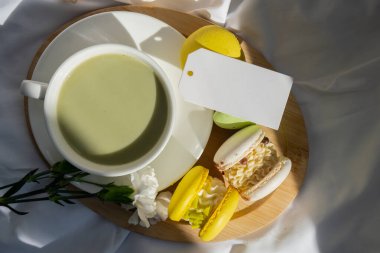 Boş mesaj kâğıdı fotokopisi: Besin zengini kibrit içeceği, ahşap tepside taze çiçeklerle süslü, modaya uygun makarna tatlısı. Günaydın güzel kahvaltı hediyesi fikri. Canlı, yaratıcı.