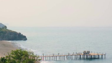 Dalgalar Antalya Türkiye 'deki ahşap iskeleye çarpıyor. Palmiyeler ve deniz seyahati turizmi konsepti. Kumsal ve dağlar. Üst görünüm. 