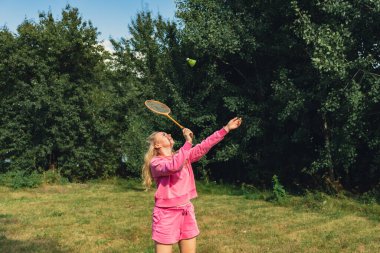 Güzel genç bir kadın açık havada Neon sarı badminton topu ve yeşil çimlerde raket oynuyor. Alternatif fitness eğlence sporu