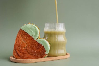 Yeşil çay Matcha latte cappuccino içeceği Sabah kahvaltısı hediye fikri Fotokopi alanlı yeşil arka planda fıstık şeklinde kruvasan. Puf puf yeni moda tatlı pastanesi. Kremalı hamur