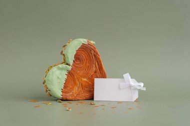 Boş kağıt nota şablonu oluşturur. Fotokopi alanı olan yeşil arka planda kalp şeklinde şam fıstıklı kruvasan. Puf puf yeni moda tatlı pastanesi. Kremalı hamur deneyi 