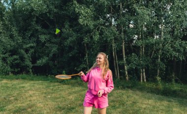 Güzel genç bir kadın açık havada Neon sarı badminton topu ve yeşil çimlerde raket oynuyor. Alternatif fitness eğlence sporu