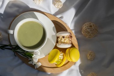 Dağınık yatağın üzerinde sarı ve beyaz badem kurabiyeli yeşil latte. Tatil kahvaltısı çay içeceği kavramı. Sıcacık minimalist süper yiyecekler canlı renkler sağlıklı beslenme. Organik kafeinsiz.