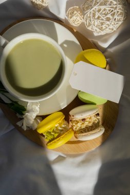 Kağıt not uzay şablonunu kopyala tatlı sarı makaron tatlı fincanı yeşil bitki bazlı kibrit çaylı latte sıcak sabah yatağı atmosferinde. Yaratıcı tatil romantik randevu fikri. Bitkisel prebiyotik lif