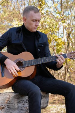 Güzel sarışın adam akustik gitar çalıyor ve şarkı söylüyor güneşli bir sonbahar gününde dışarıda eğleniyor. Sanatçı müzik aleti öğreniyor ve pratik yapıyor. Sonbahar mevsimsel havayı terk eder 