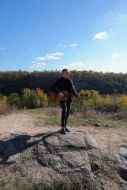 Sonbahar ormanında dışarıda gitar çalan sarışın bir adam. Ses terapisi, akıl sağlığı ve sağlık ayinleri kavramı. Sakinlik sükuneti ses duyusal uygulamaları. Aura tarım enerjisi bütünsel