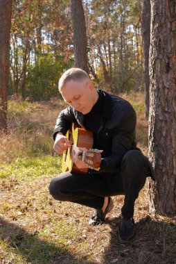 Sonbahar ormanında dışarıda gitar çalan sarışın bir adam. Ses terapisi, akıl sağlığı ve sağlık ayinleri kavramı. Sakinlik sükuneti ses duyusal uygulamaları. Aura tarım enerjisi bütünsel