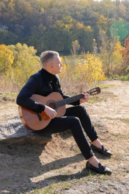 Sonbahar ormanında dışarıda gitar çalan sarışın bir adam. Ses terapisi, akıl sağlığı ve sağlık ayinleri kavramı. Sakinlik sükuneti ses duyusal uygulamaları. Aura tarım enerjisi bütünsel