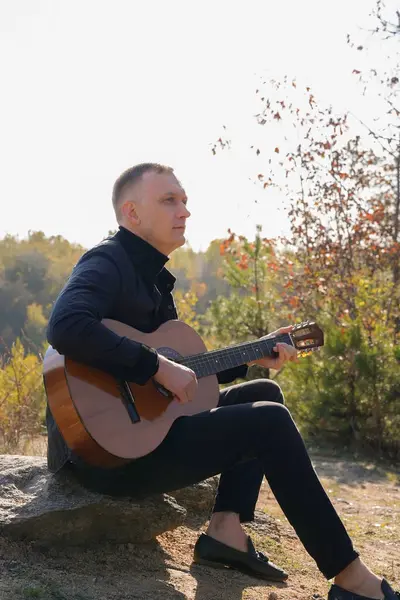 Gülümseyen beyaz ressamın portresi sonbahar parkında ahşap akustik gitar çalar. Genç söz yazarı, sonbahar zamanı dışarıda telli müzik aleti hobisi yapıyor. Sesli müzik doğal olarak iyileşir.