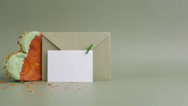 Zarflı tebrik kartı maketli boş bir şablon kağıdı. Fotokopi alanı olan yeşil arka planda kalp şeklinde şam fıstıklı kruvasan. Puf puf yeni moda tatlı pastanesi. Kremalı hamur