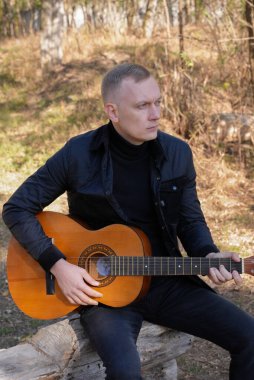 Sonbahar ormanında dışarıda gitar çalan sarışın bir adam. Ses terapisi, akıl sağlığı ve sağlık ayinleri kavramı. Sakinlik sükuneti ses duyusal uygulamaları. Aura tarım enerjisi bütünsel