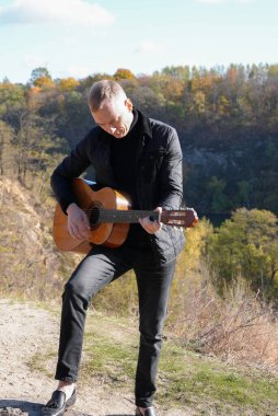 Sonbahar ormanında dışarıda gitar çalan sarışın bir adam. Ses terapisi, akıl sağlığı ve sağlık ayinleri kavramı. Sakinlik sükuneti ses duyusal uygulamaları. Aura tarım enerjisi bütünsel