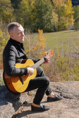 Sonbahar ormanında dışarıda gitar çalan sarışın bir adam. Ses terapisi, akıl sağlığı ve sağlık ayinleri kavramı. Sakinlik sükuneti ses duyusal uygulamaları. Aura tarım enerjisi bütünsel