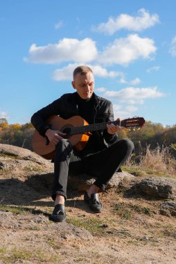 Sonbahar ormanında dışarıda gitar çalan sarışın bir adam. Ses terapisi, akıl sağlığı ve sağlık ayinleri kavramı. Sakinlik sükuneti ses duyusal uygulamaları. Aura tarım enerjisi bütünsel