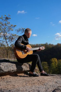 Güzel sarışın adam akustik gitar çalıyor ve şarkı söylüyor güneşli bir sonbahar gününde dışarıda eğleniyor. Sanatçı müzik aleti öğreniyor ve pratik yapıyor. Sonbahar mevsimsel havayı terk eder 