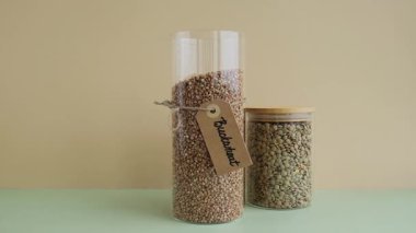 Tanınmayan bir kadın, yenilenebilir cam kavanozu çiğ karabuğday ve yeşil mercimek lapasıyla dolduruyor. Ürün formatında çevre dostu yaşam. Yeniden kullanılabilir konteynır dolduruluyor Yazılan tüm tahıl türleri