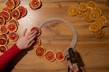 Kurutulmuş portakal dilimlerinden elde yapılan el yapımı Noel çelengi kullanan bir kadın. Tatil hazırlığı, yaratıcı dekorasyon ustası sınıfı. Etkin faaliyetler sürdürülebilir sorumluluk