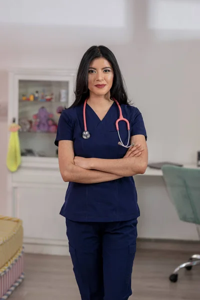 Young Latina doctor, looking at the camera with her arms crossed, in her medical office.