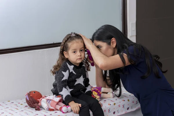 doctor checks a little girl's ear with an otoscope, in her medical practice