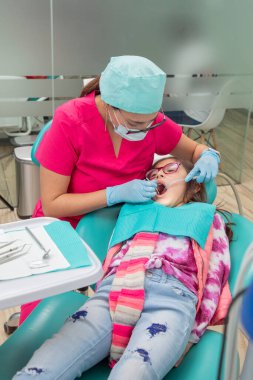 vertical image of a dentist checking a girls mouth in her office.