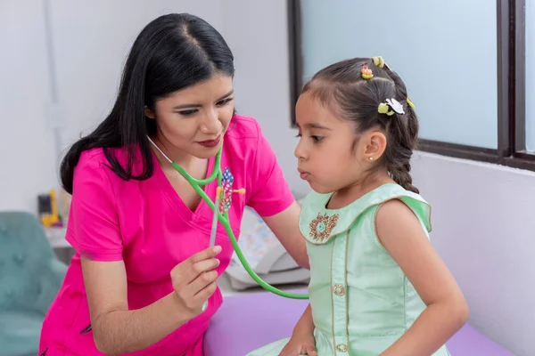 小児科医は女の子の肺をチェック 聴診器で彼女を調べながら 彼女の打撃をピンホイールに持っている — ストック写真