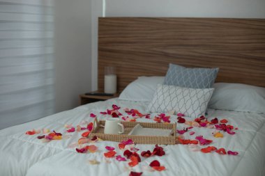 Gül yaprakları ve servis tepsisiyle süslenmiş bir otel yatağı. Lüks otel, konaklama ve seyahat konsepti