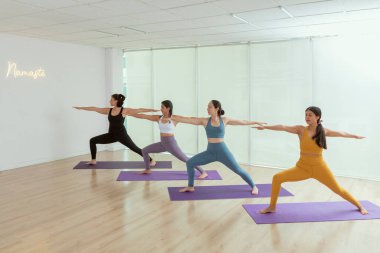 Yoga sınıfındaki bir grup kadın savaşçı pozu veriyor.