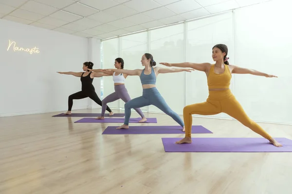 Yoga sınıfındaki bir grup kadın savaşçı pozu veriyor.