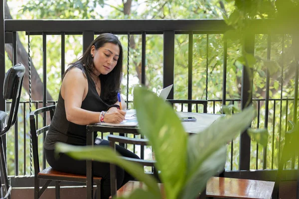 A woman writes in her diary while working on the terrace of a coffee shop
