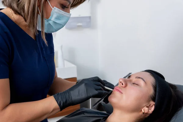 一位美容师医生测量一位年轻妇女的嘴唇 给她注射透明质酸疗法 — 图库照片