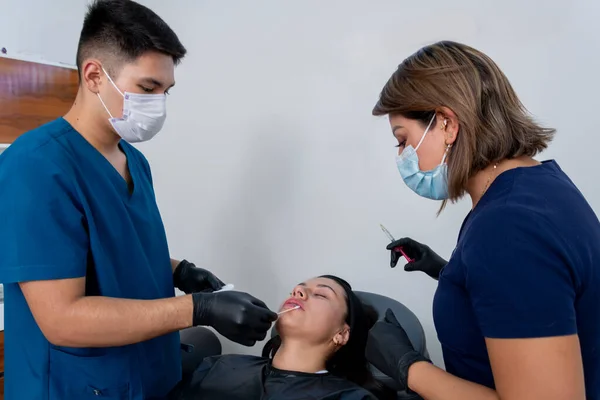 一位美容师和她的助手正要给一位年轻女子的嘴唇注射透明质酸 — 图库照片