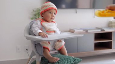 Sandalyesinde oturan bir bebek kahvaltıda yemeğini evde yer. Bebek sütten kesme konsepti
