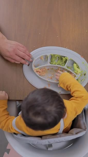 ベイビーはウィーニングコンセプトを導いた 木のテーブルの上にあるシリコンプレートから食べる赤ちゃんの手のトップビュー — ストック動画