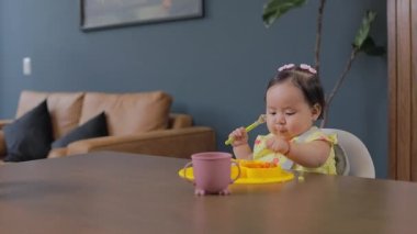 Bebek evde elleriyle yemek yiyor ve diğer elinde kaşık tutuyor. Bebek sütten kesilme konseptine öncülük ediyor.
