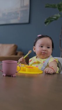 Evde masada oturan Latin bir bebek tabağı ve silikon bardağıyla yemek yiyor. Bebek sütten kesme konsepti