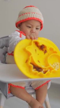 Latin bebek evde kahvaltısını yaparken yemek tabağıyla oynuyor. Sandalyesinde oturuyor. Bebek sütten kesme konsepti