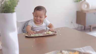 Latin bebek kahvaltı ederken gülümsüyor ve önceden doldurulmuş bir kaşık alıyor. Latin bir bebeğin tamamlayıcı beslenmesi. BLW