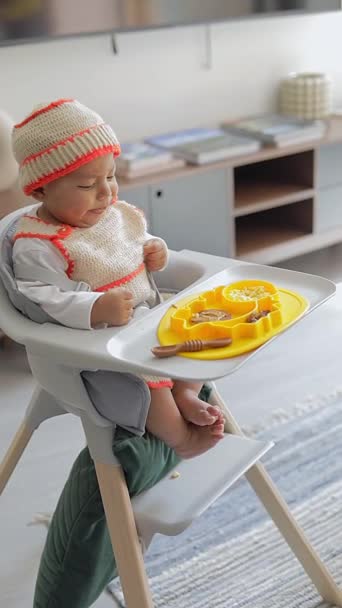 ブループレートで椅子に座って朝食を食べているラテン系の赤ちゃんの補給 — ストック動画