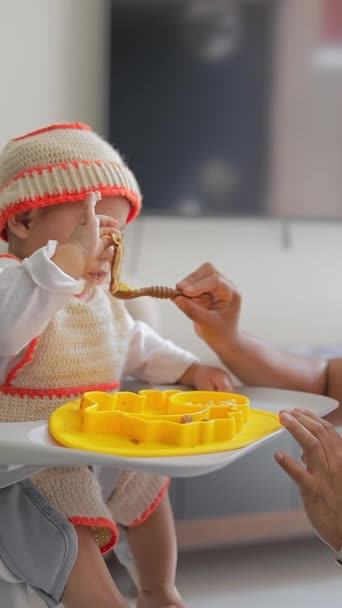 一只手拿着勺子的拉丁婴儿正坐在椅子上吃早餐 他的嘴里衔着一只勺子给他食物 — 图库视频影像