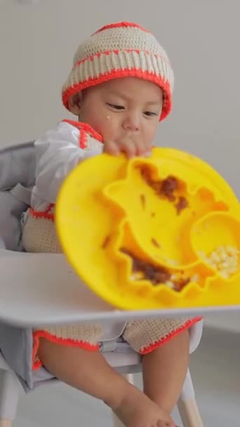 ラティーノの赤ちゃんは 椅子に座って自宅で朝食をとっているときに食べ物の皿で遊んでいます 赤ちゃんはウィーニングコンセプトを導きました — ストック動画