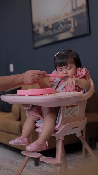 食べるために椅子に座っている少女は食欲の欠如のために食べ物を捨て 彼女のお父さんはスプーンで彼女を養おうとします — ストック動画